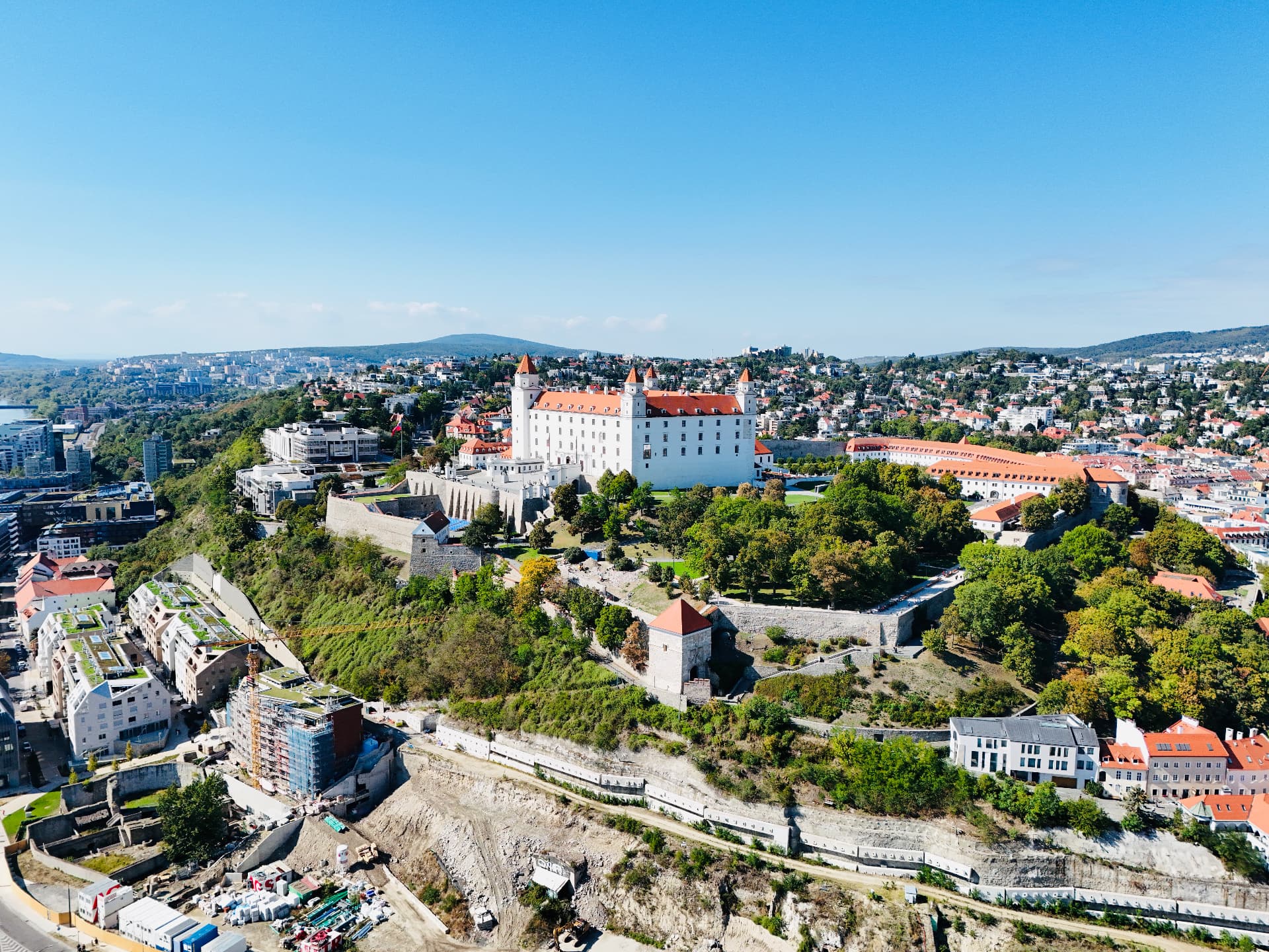 Aerial view of white Bratislava Castle above the city, surrounded by fortified walls, autumn trees and red-roofed buildings